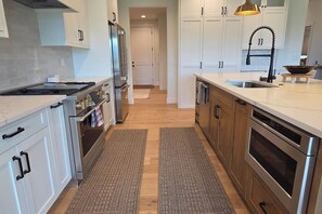 A modern kitchen with stainless steel appliances, white cabinetry, and a wooden floor. - Teton Reserve Royal Elk Lodge (Victor)