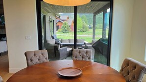 Ein runder Holztisch mit vier gepolsterten Stühlen, eine Glastrennwand und Blick auf eine Außenpatio mit Sitzgelegenheiten und Grillplatz.