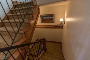 A wooden staircase with a metal railing, a painting on the wall, and a small shelf with decorative items.