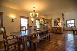 A spacious dining area with a long wooden table and benches, surrounded by windows and a chandelier.