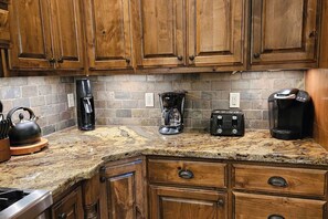 A kitchen with wooden cabinets, a granite countertop, a kettle, a coffee maker, a toaster, and a Keurig coffee machine.