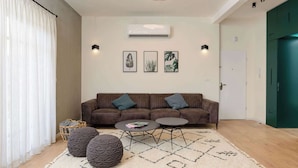Un salon moderne avec un canapé marron, deux poufs ronds, une table basse et un tapis à motifs.