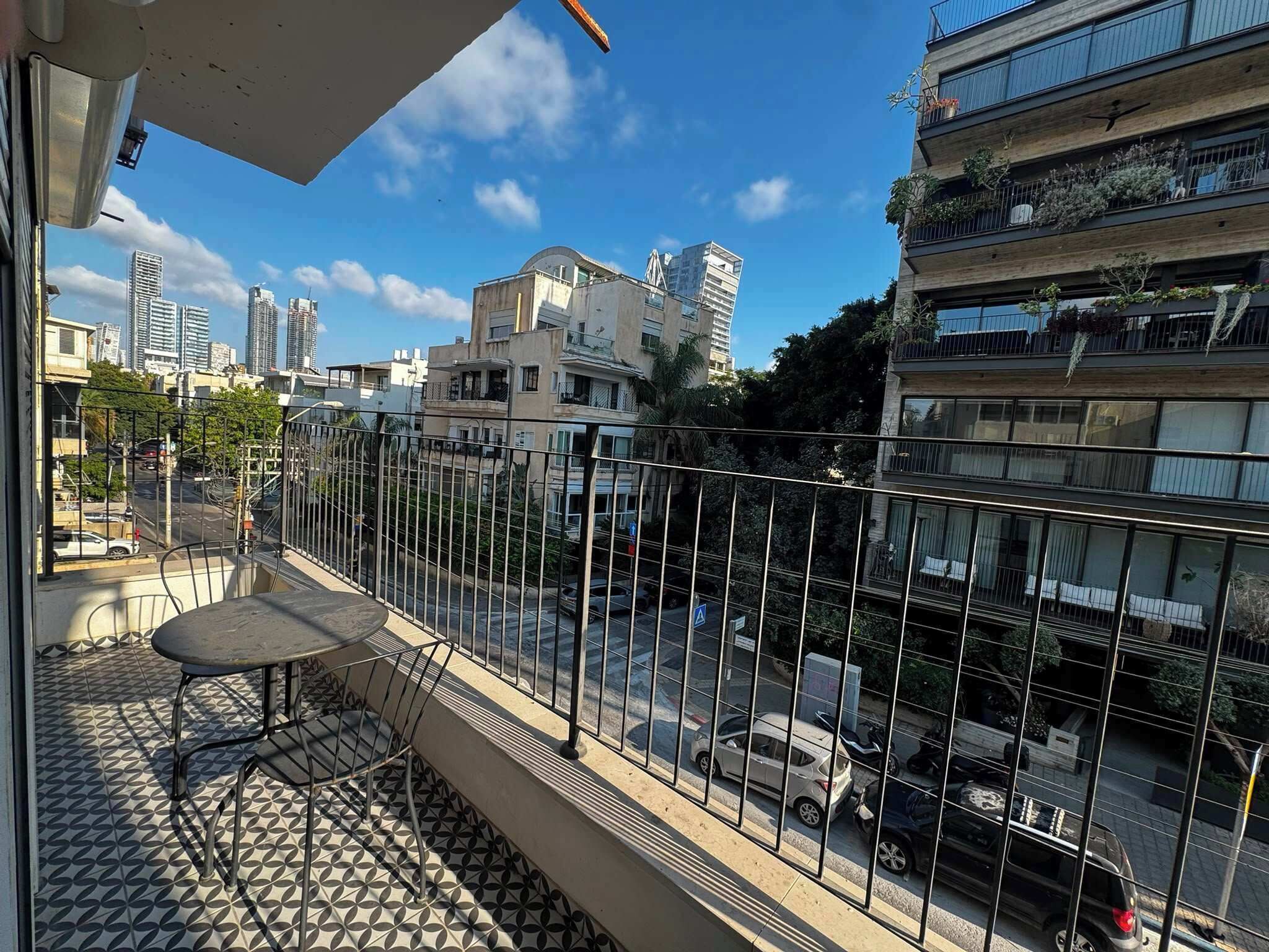 A balcony with a patterned floor, a metal railing, and a table with chairs.