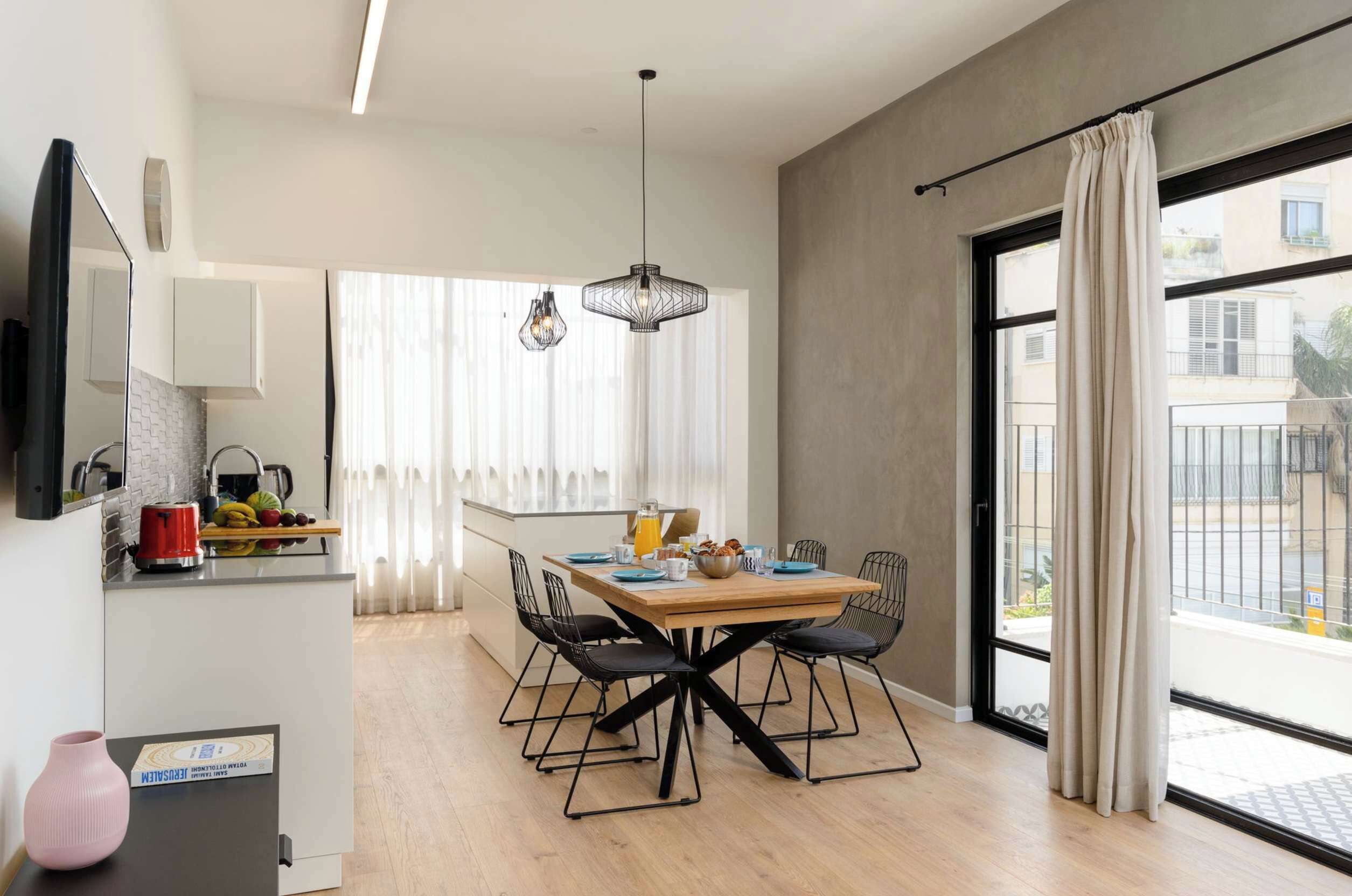 A modern kitchen with a dining area, a large window with curtains, and a view of the outside.