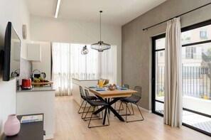 A modern kitchen with a dining area, a large window with curtains, and a view of the outside. - Modern 2BR with Sunny Balcony by HolyGuest (Tel Aviv-Yafo)