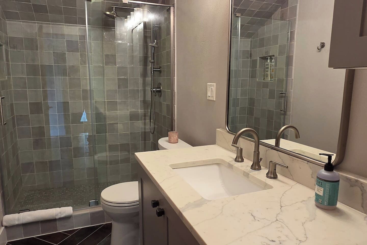 A bathroom with a glass-enclosed shower, a sink with a marble countertop, and a toilet.