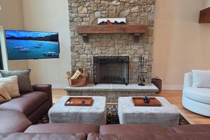 A living room with a stone fireplace, a television mounted on the wall, and a white sofa.