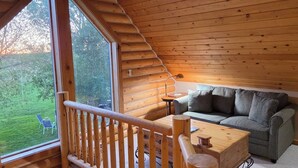 Interior acogedor de una cabaña con techo de madera, un sofá, una mesa y vistas a un paisaje verde.