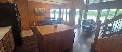 A spacious kitchen with wooden cabinets and a large island, leading to a dining area with a view of a lake.