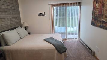 A bedroom with a bed, a nightstand, a lamp, a window with blinds, and a painting on the wall.