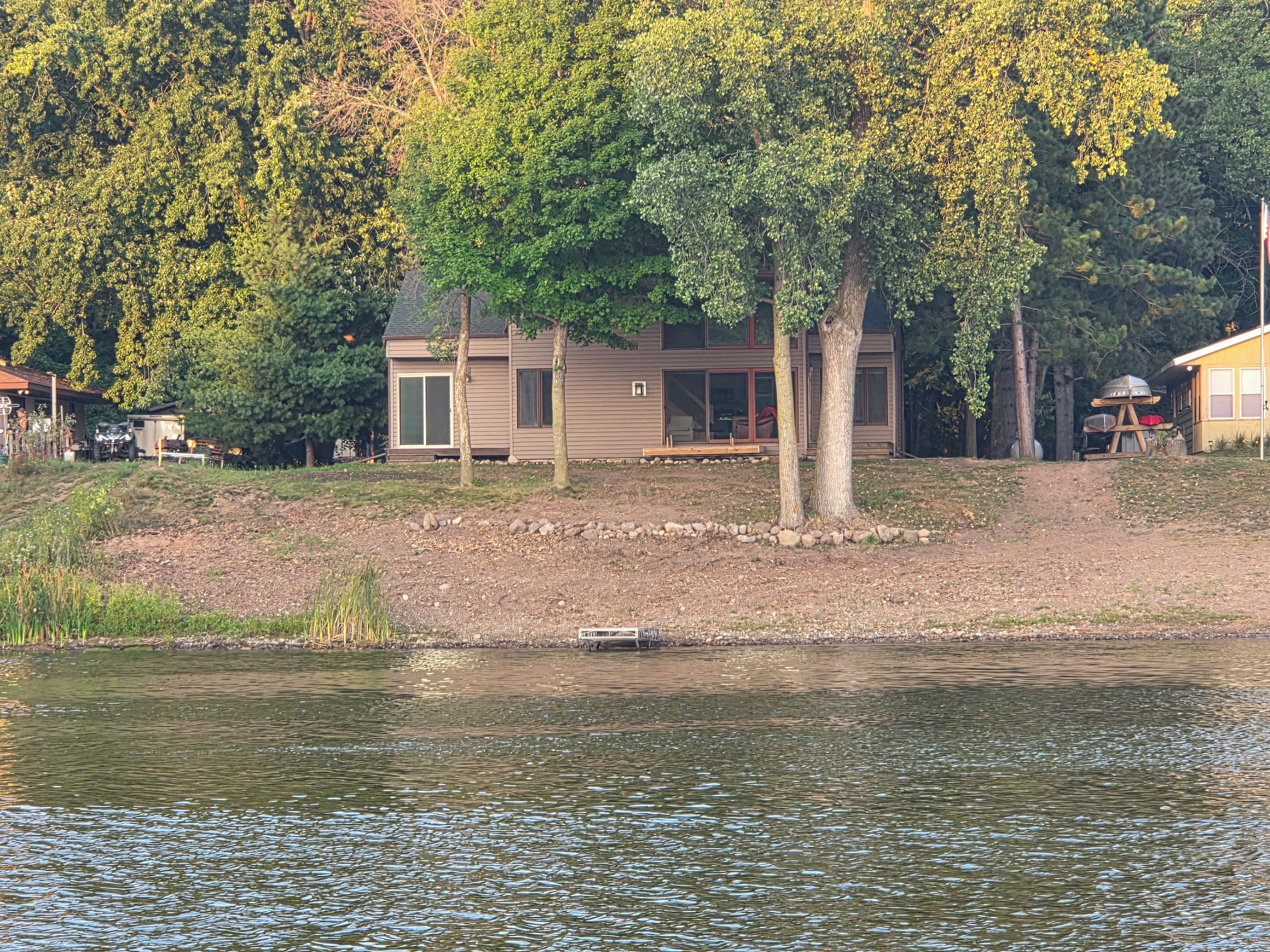 Un chalet au bord du lac, doté d’une terrasse, entouré d’arbres et agrémenté d’un quai.