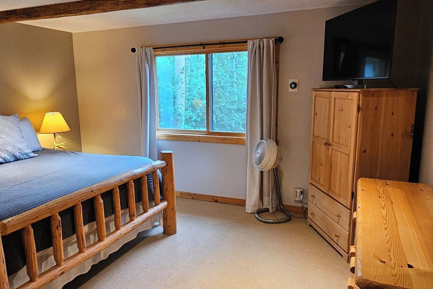 Quarto com uma cama, cómoda de madeira, televisão e janela com cortinas.