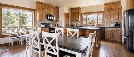 A spacious kitchen with wooden cabinets, a central island, and a dining area with white chairs.