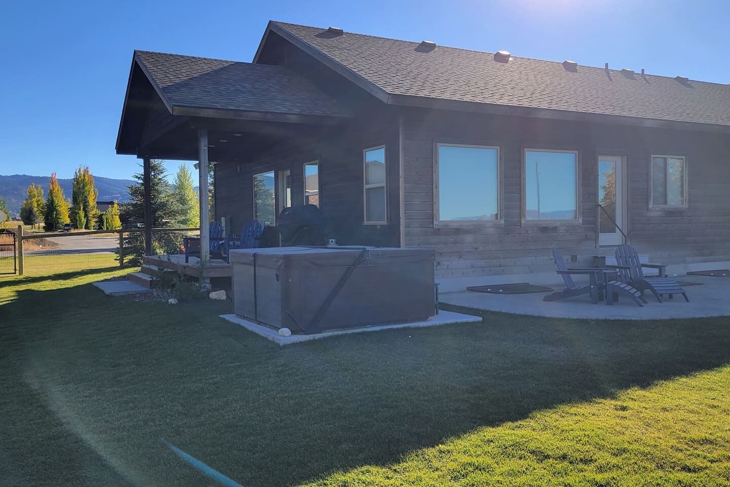 A modern house with a covered patio, a hot tub, and a well-maintained lawn.