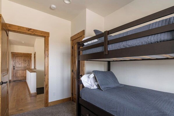 A bunk bed with a lower bunk and a single bed, a wooden door, and a hallway leading to a kitchen area. - Retreat on the Edge of Victor with New Hot Tub (Victor)