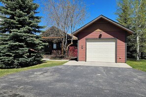 A residential property with a red garage, a driveway, and a large evergreen tree. - Teton Creek Resort Home (Driggs)