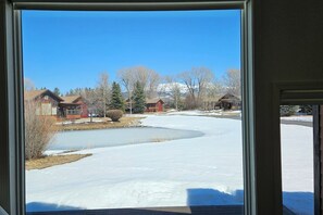 Blick durch ein Fenster auf eine Wohngegend mit Häusern, einem schneebedeckten Feld und blauem Himmel.