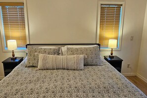 A bed with a patterned bedspread, two nightstands with lamps, and a window with blinds. - Teton Creek Resort Home (Driggs)