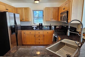 A kitchen with wooden cabinets, a stainless steel refrigerator, a sink with a modern faucet, and a window providing natural light. - Teton Creek Resort Home (Driggs)