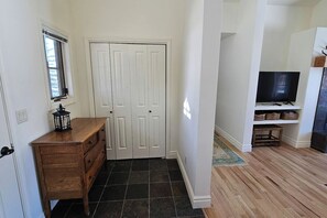 A hallway with a wooden dresser, a closed white door, a television on a stand, and a patterned rug. - Teton Creek Resort Home (Driggs)