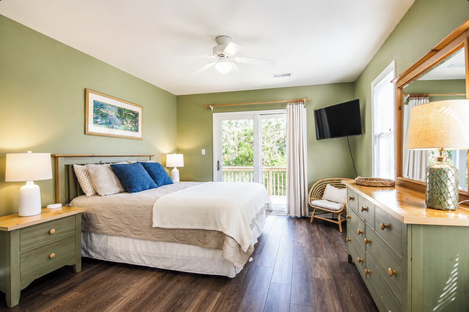 A bedroom with a bed, bedside tables, a chair, a dresser, a ceiling fan, a TV, and a window with curtains.