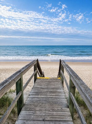 A wooden boardwalk leading to a beach with a clear sky.
