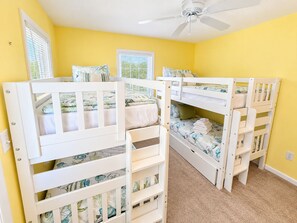 A room with bunk beds, a ceiling fan, and two windows with blinds.