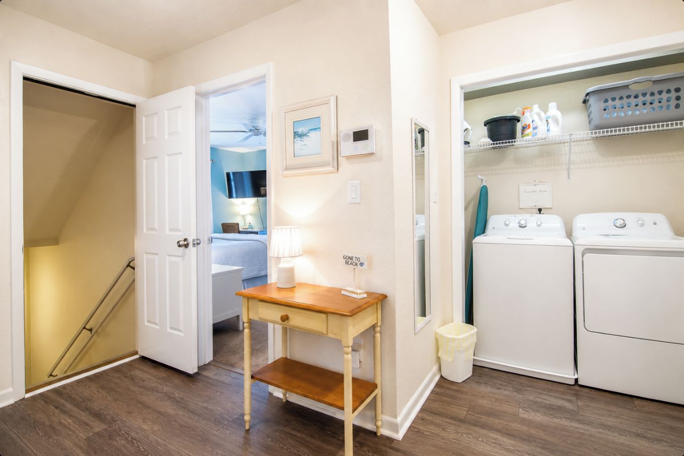 A laundry room with two washing machines, a drying rack, and a small table with a lamp.