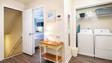 A laundry room with two washing machines, a drying rack, and a small table with a lamp.