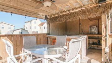 An outdoor patio with a round table and chairs, a ceiling fan, and a thatched roof.