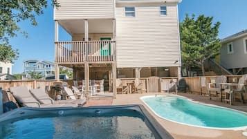 A two-story house with a backyard pool, outdoor furniture, and a wooden deck.
