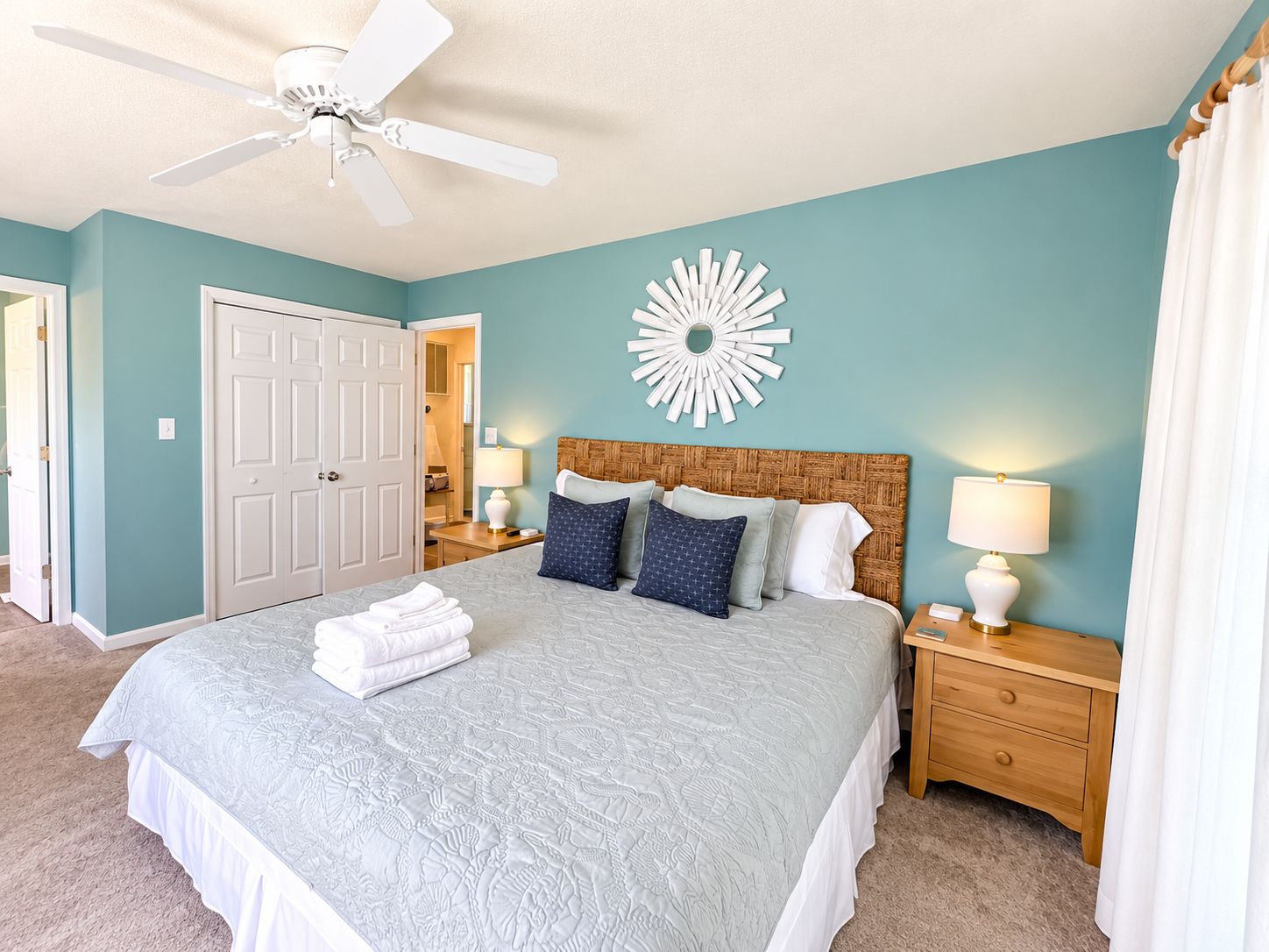 A bedroom with a bed, nightstands, a ceiling fan, a door, and a wall decoration.