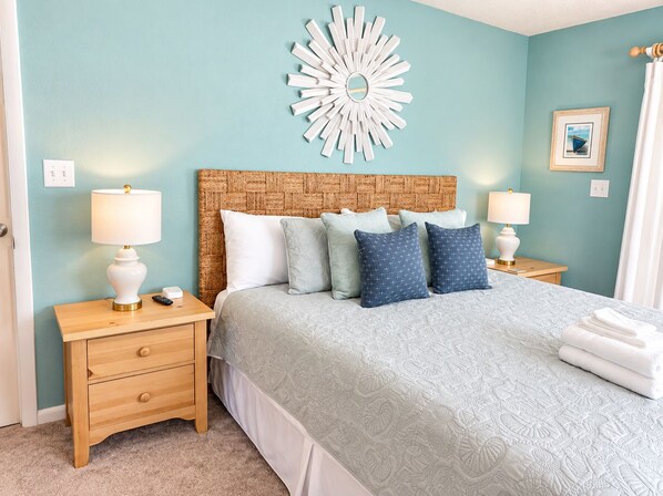 A bedroom with a bed, two nightstands, a wall clock, and a decorative mirror. - Private Pool · 3-Min Walk to Beach · Sleeps 8, Loaded, Pets OK (Nags Head)