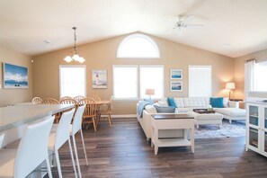 A spacious living area with a dining table, white sofas, and a kitchen area.