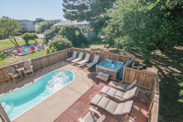 A backyard with a swimming pool, lounge chairs, and a hot tub.