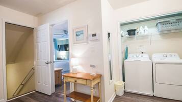 A laundry area with two washing machines, a small table, and a trash can.