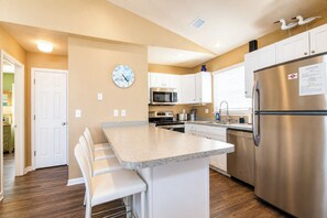 A modern kitchen with white cabinets, stainless steel appliances, and a central island with bar stools. - Private Pool · 3-Min Walk to Beach · Sleeps 8, Loaded, Pets OK (Nags Head)