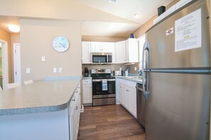 A compact kitchen with stainless steel appliances, white cabinetry, and a wooden floor.