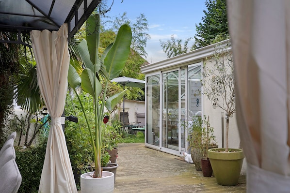 A conservatory with glass walls, potted plants, and a wooden deck.