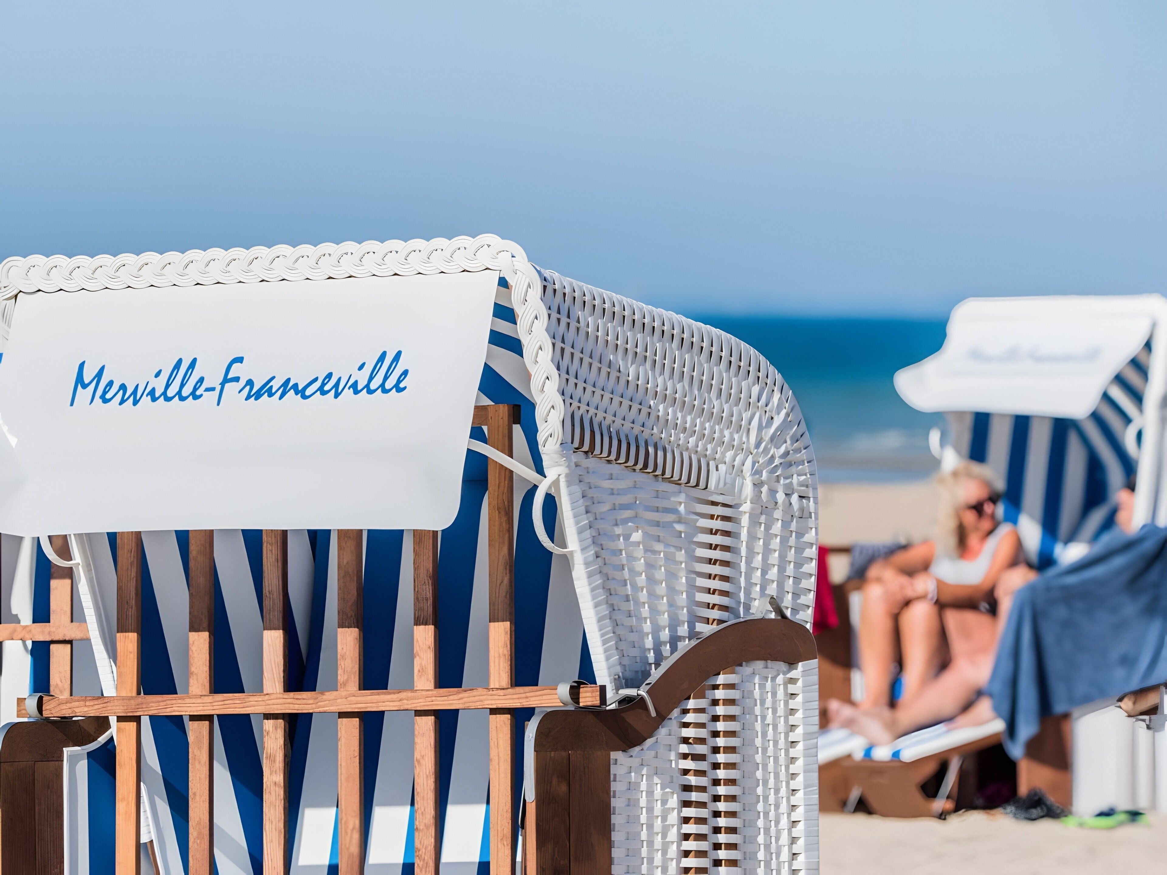 Una silla de playa con un cartel que dice 'Merville-Franceville' y una sombrilla a rayas de fondo.