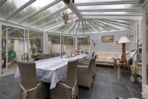 A conservatory with a dining table, wicker chairs, a sofa, and a lamp. - Bed and Breakfast 'Chambre 2' with Shared Terrace, Shared Garden and Wi-Fi (Merville-Franceville-Plage)
