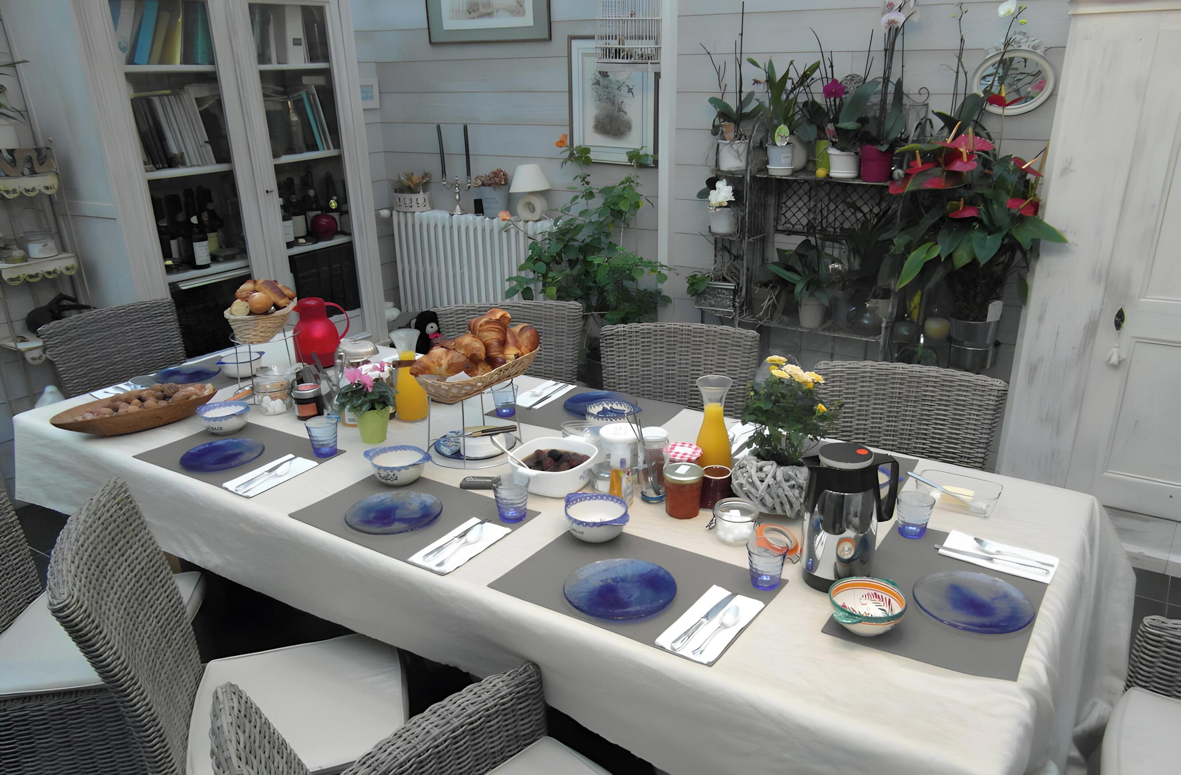 Una mesa de comedor dispuesta con varios platos, cubiertos y una cafetera, rodeada de sillas de mimbre.