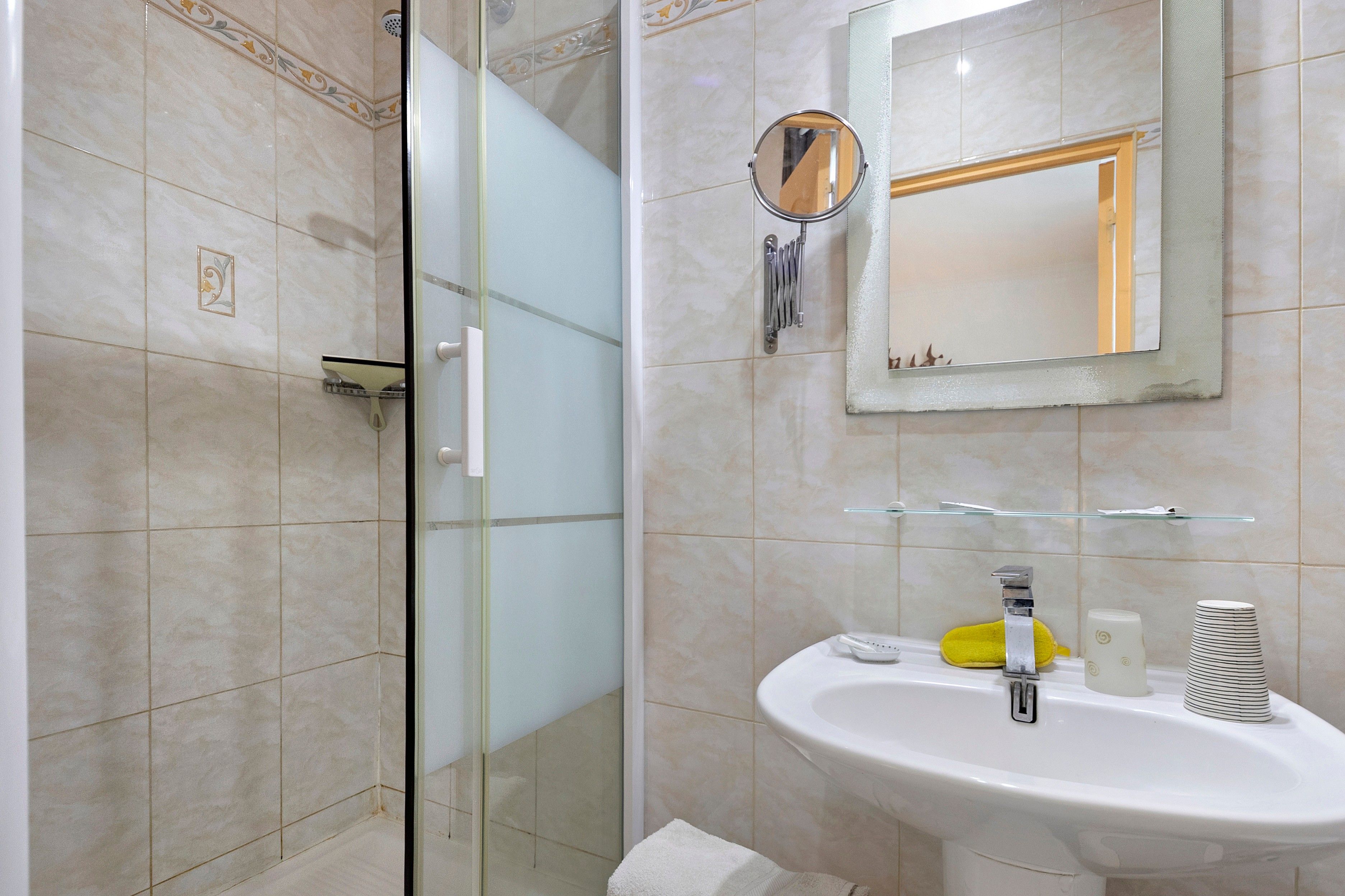 Een badkamer met een douchecabine van glas, een wastafel met spiegel erboven en een handdoekrek.