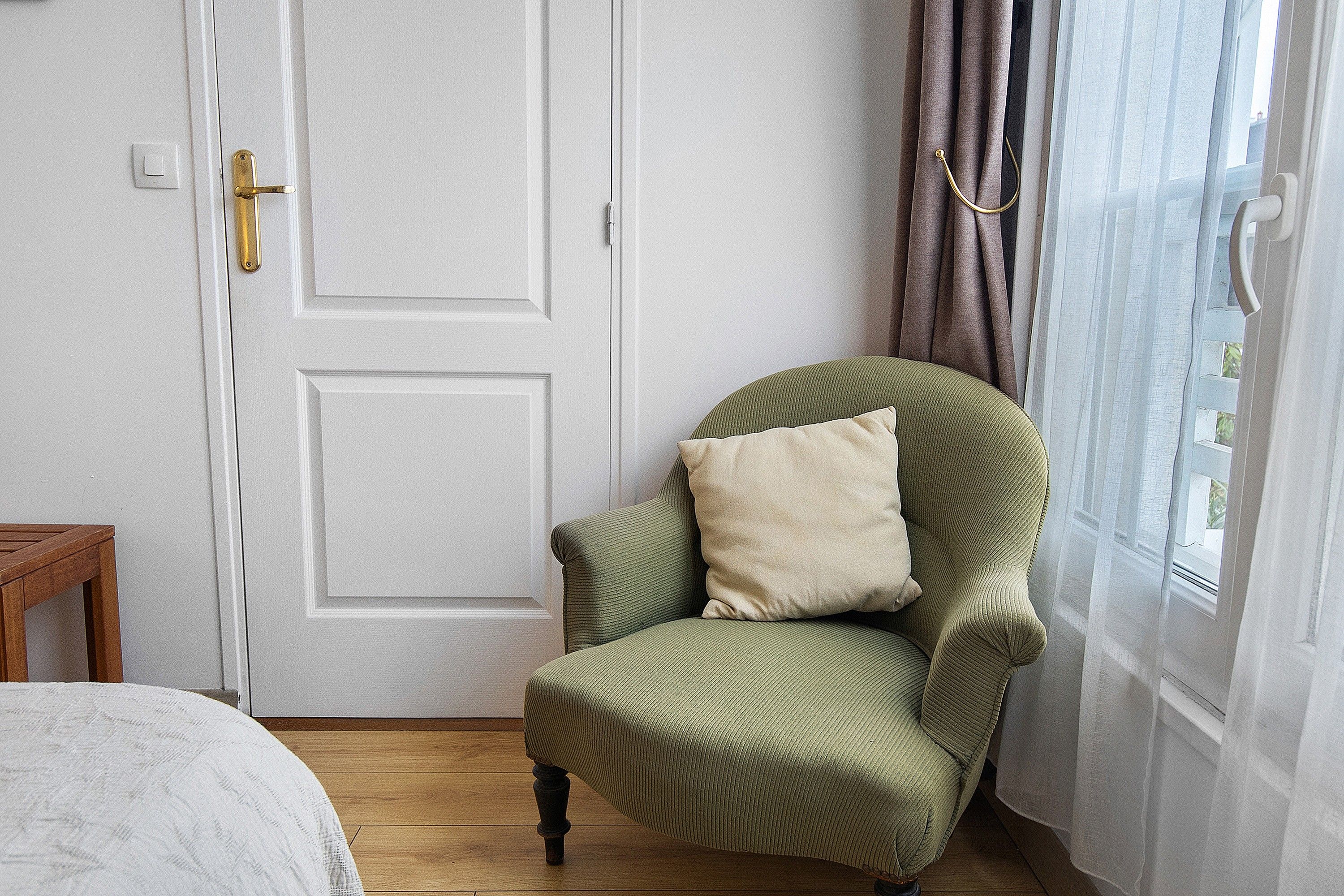 Een kamer met een groene bekleden fauteuil, een witte deur en een raam met gordijnen.
