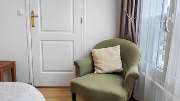 Een kamer met een groene bekleden fauteuil, een witte deur en een raam met gordijnen.