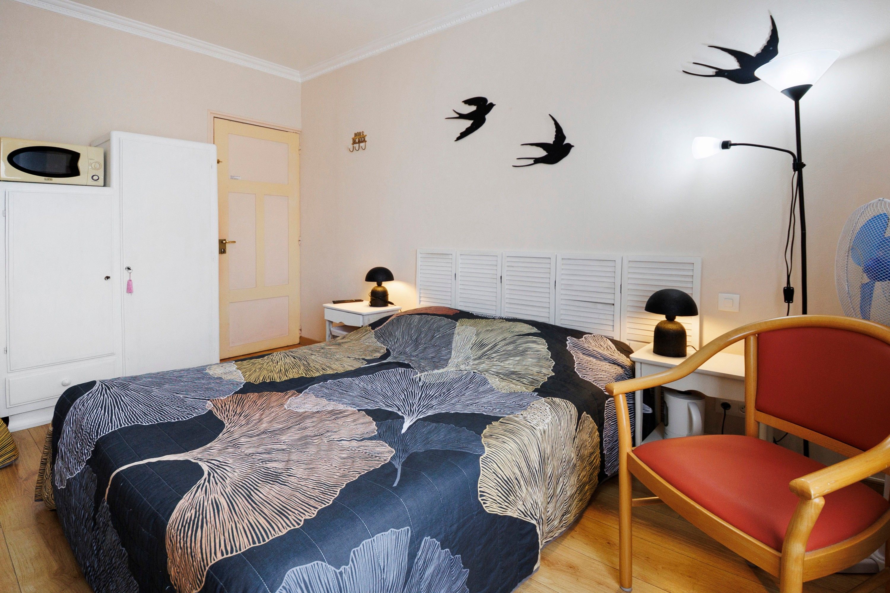 Quarto com cama, cadeira, escrivaninha, abajur e parede com silhuetas de pássaros.