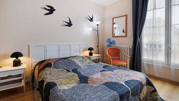 Une chambre à coucher comprenant un lit, une chaise, un bureau, une lampe, un radiateur et une fenêtre avec des rideaux.