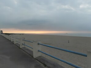 Une promenade en bord de mer, dotée d’une rambarde, qui mène à une plage de sable.