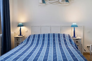 A bedroom with a bed, two bedside tables, a nightstand, a lamp, and a wall-mounted light fixture.