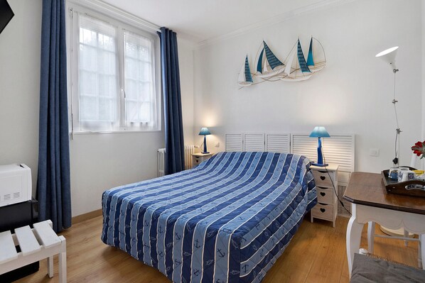 A bedroom with a bed, a desk, a chair, a radiator, and a window with curtains.